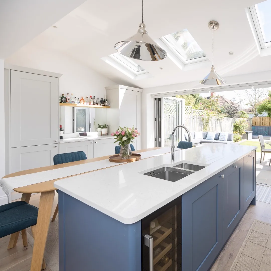 Open-plan kitchen in the rear extension with a navy island, roof windows, polished pendant lights and bi-fold doors open to the garden